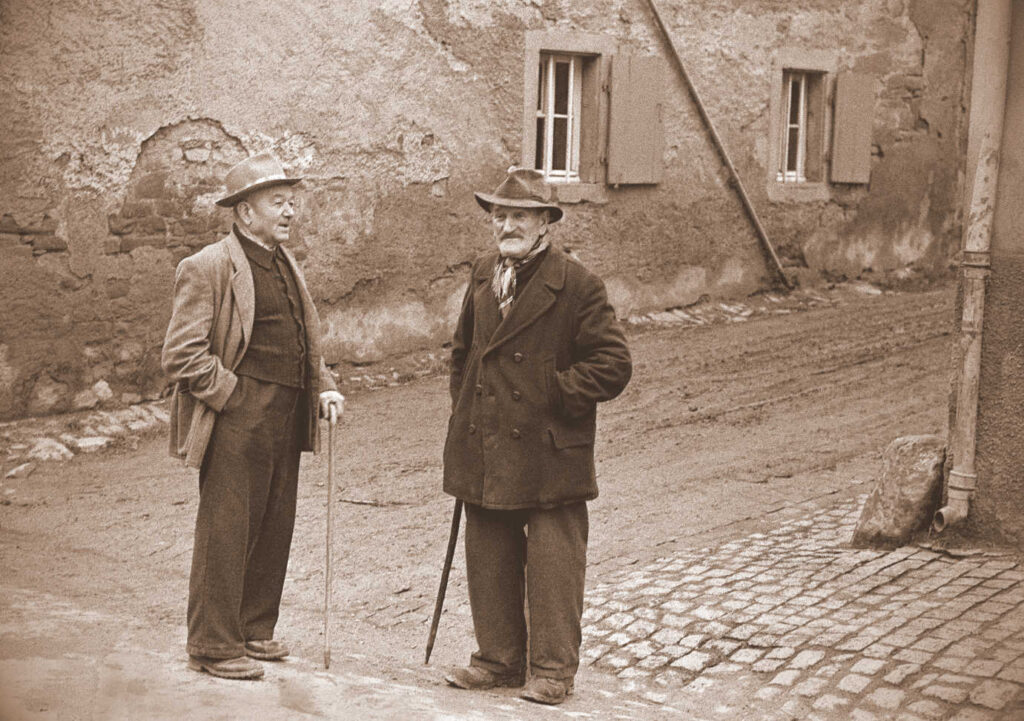Two men standing on the sidewalk conversing, Germany 1957.